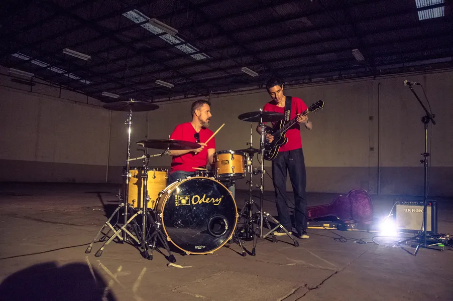 Gabriel e Samuel com guitarra e bateria em um espaço de apresentação